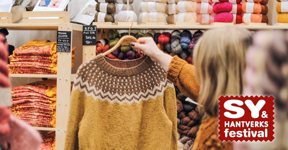 Person h�ller upp en stickad tr�ja och kollar p�, p� sy och hantverksfestivalen